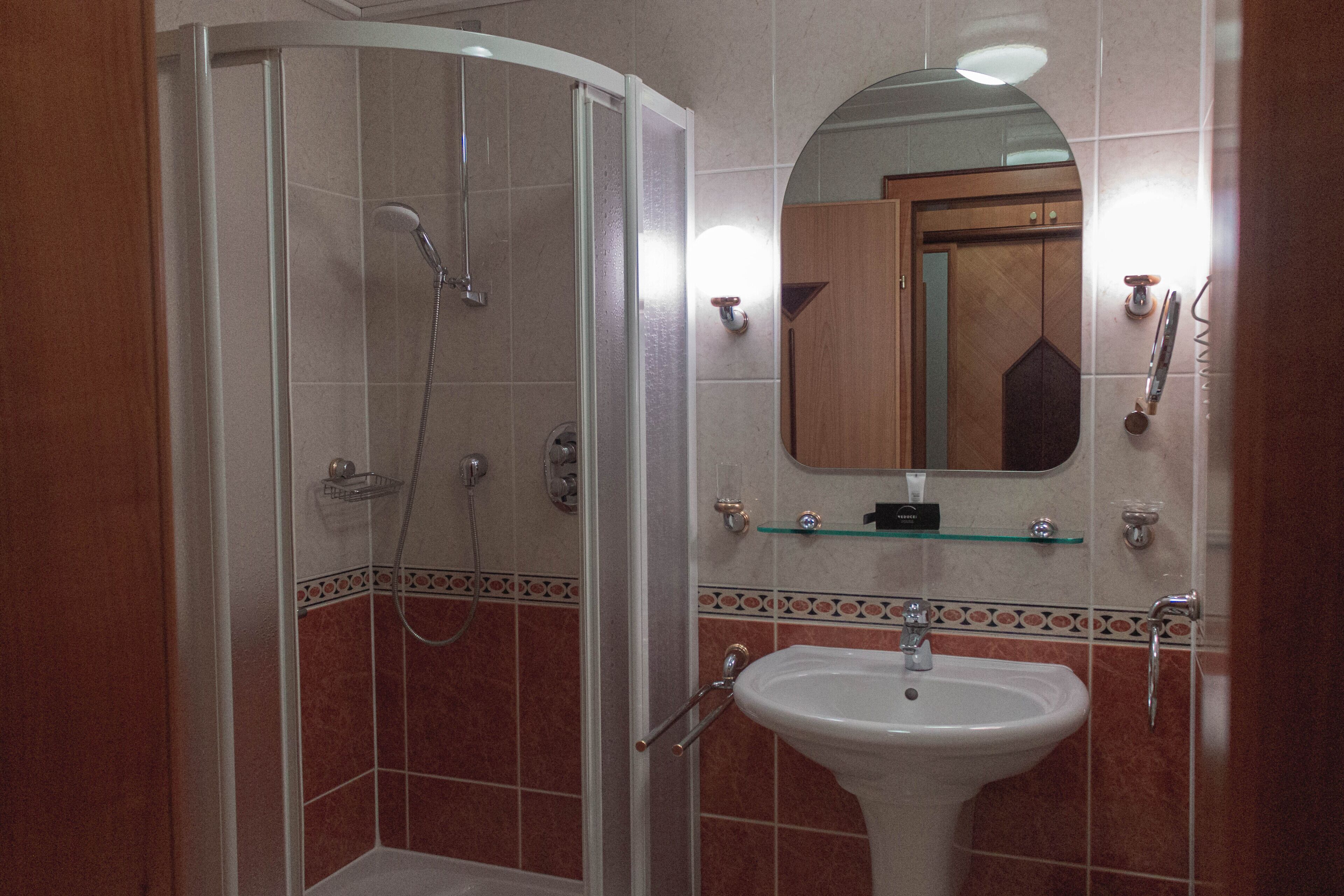 Een badkamer met een douchecabine, een wastafel en een spiegel erboven.