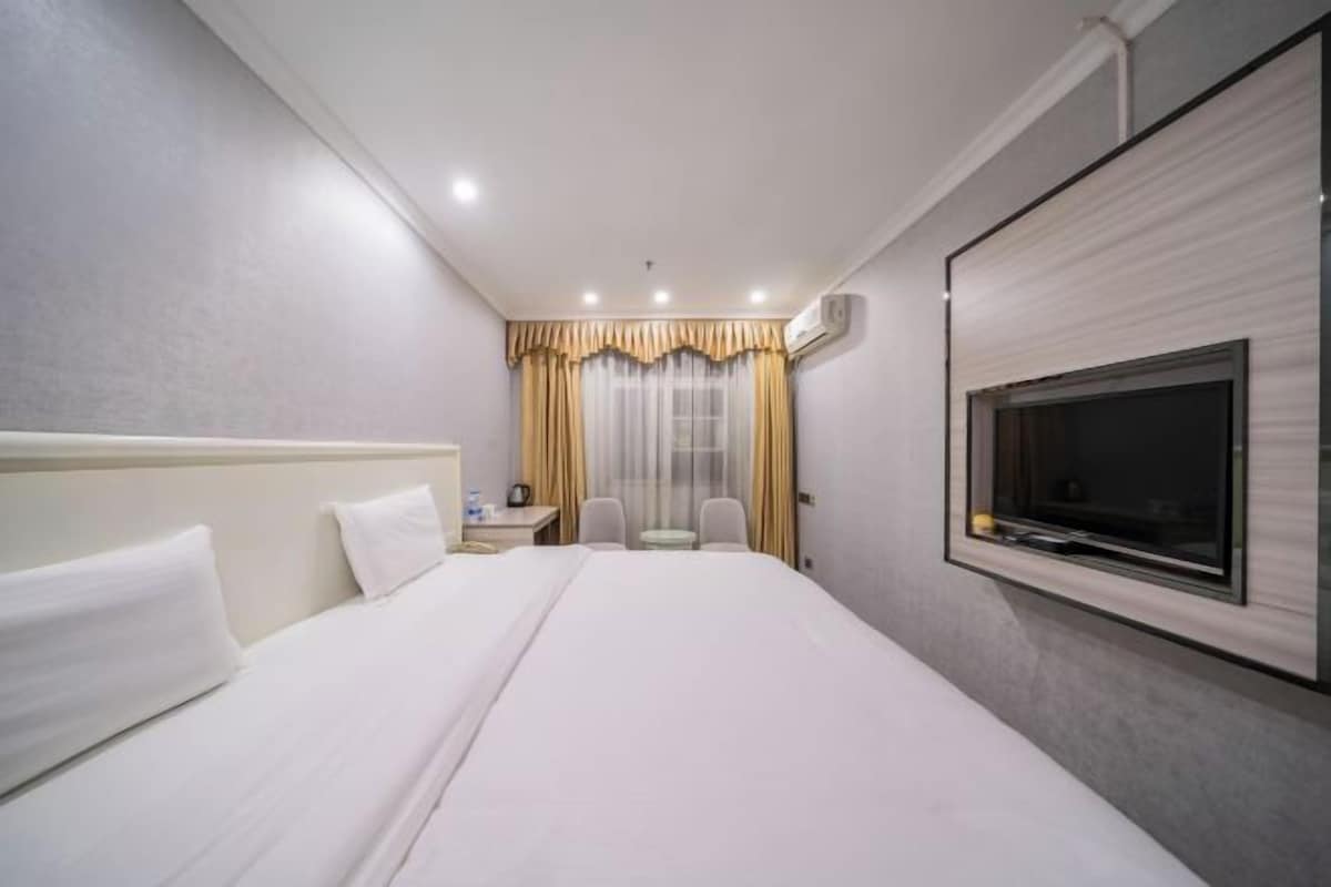 Una camera d'hotel con un letto grande, una TV a parete, un tavolino con una sedia e una finestra con tende.
