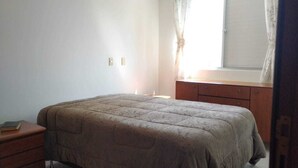 Un dormitorio con cama, mesita de noche, cómoda y ventana con cortinas.