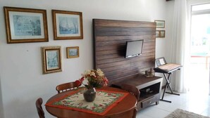 Un comedor con mesa de madera, sillas, un florero con flores y un televisor instalado en una pared de paneles de madera.