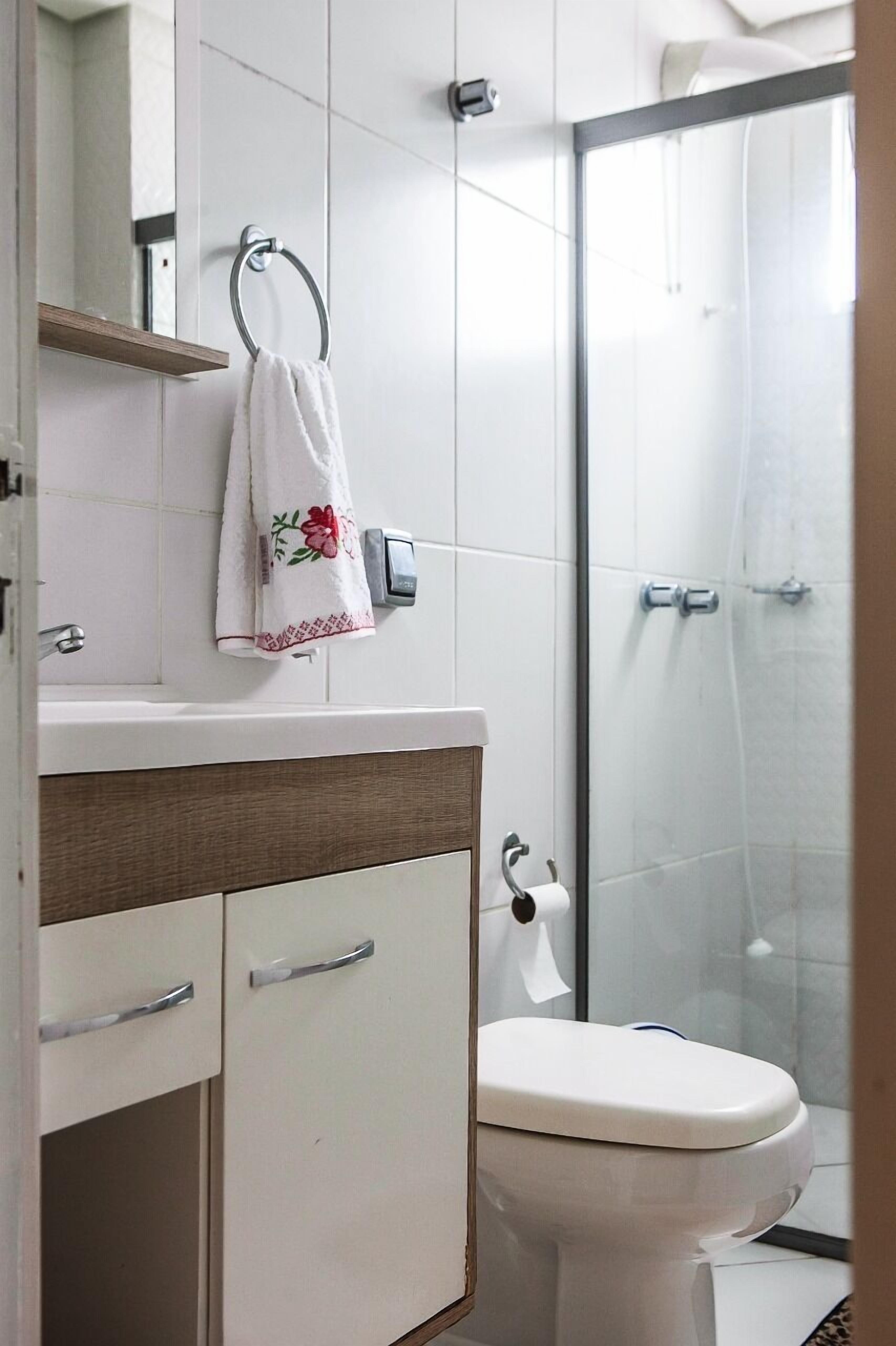 A bathroom with a toilet, a sink with a mirror, a towel hanging on a ring, and a shower area.