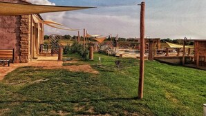 A courtyard with a stone building, a wooden bench, and a grassy area with a water feature. - Resort Fonte Vulci (Canino)