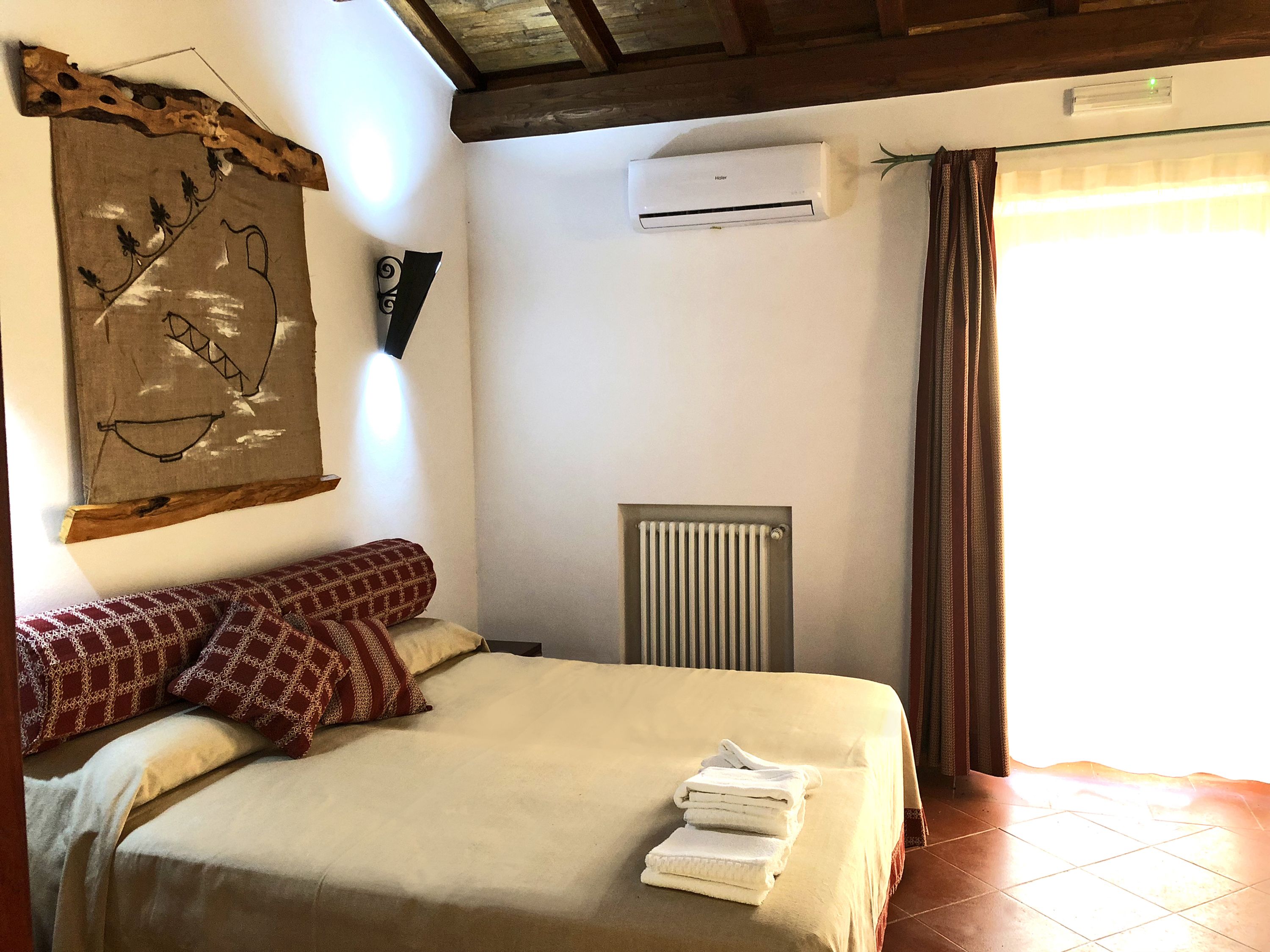 Quarto com cama, radiador, aparelho de ar condicionado e uma pintura grande na parede.