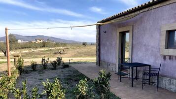 Un patio con mesa y sillas, una pérgola y vistas a montañas lejanas.