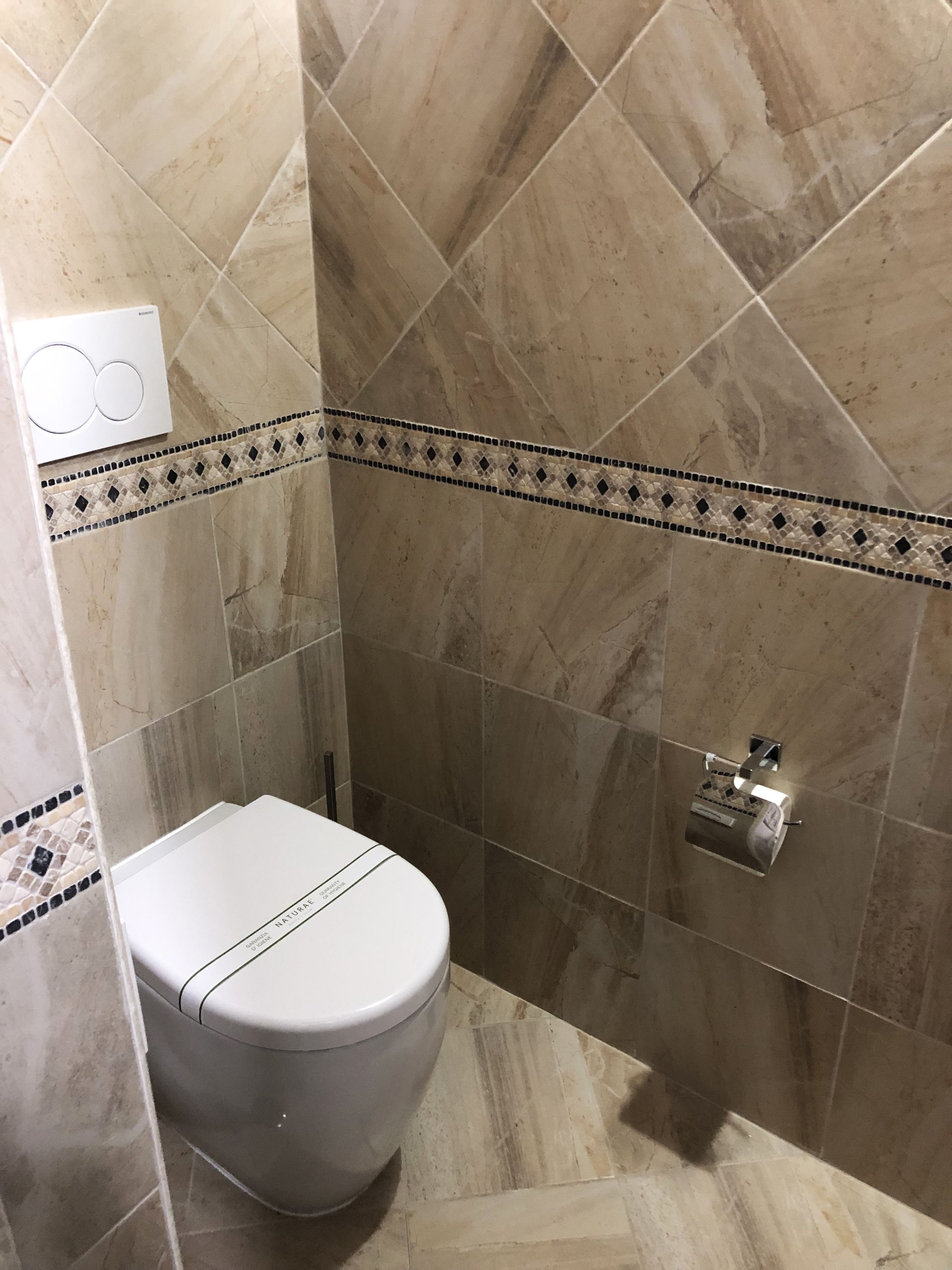 A bathroom with a toilet, a shower area, and a wall-mounted towel dispenser.