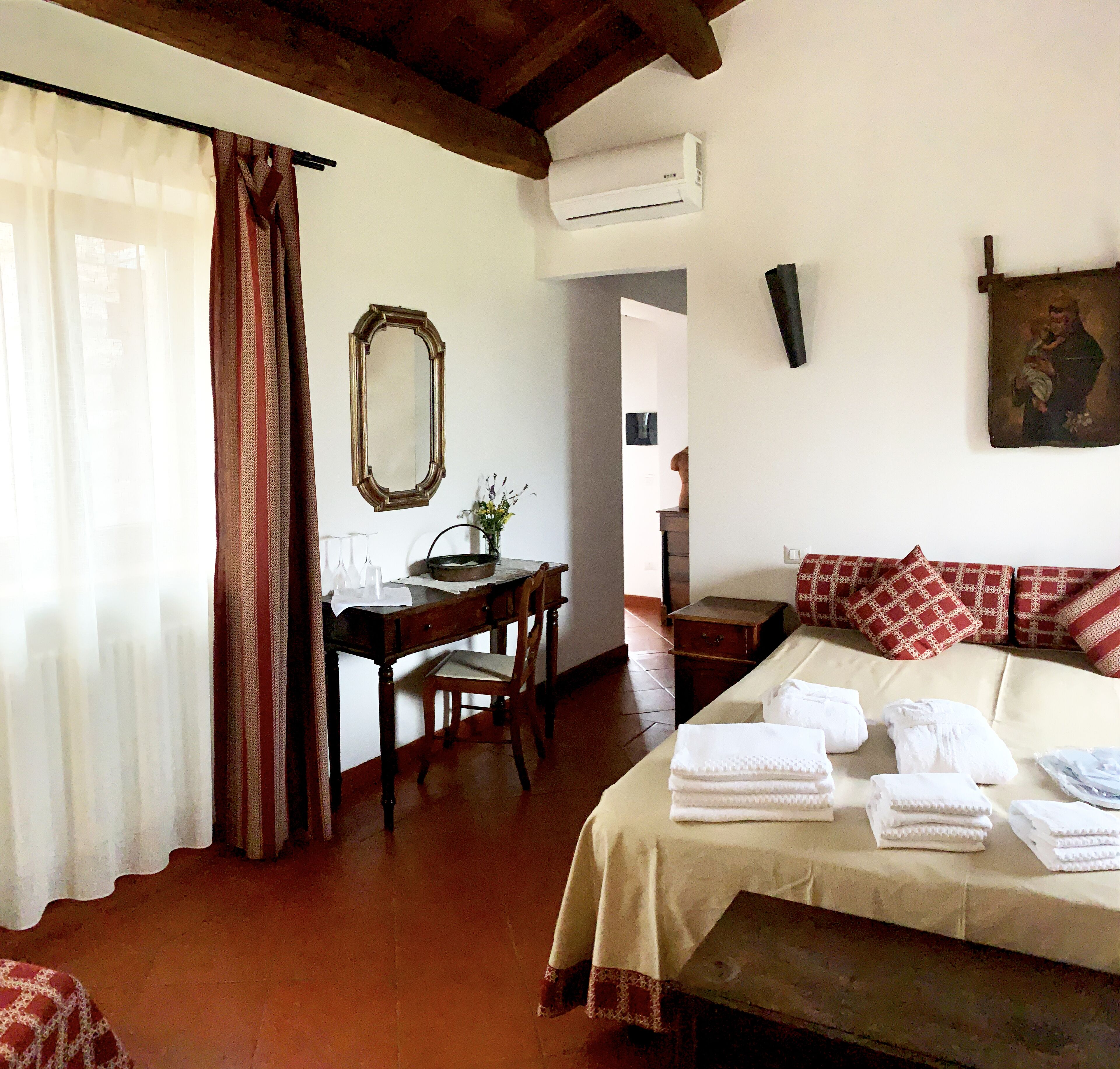 Una habitación con cama, escritorio, silla, espejo y un cuadro en la pared.