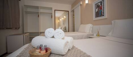 A hotel room with two beds, a large mirror, a wall-mounted artwork, and a bedside table with toiletries.