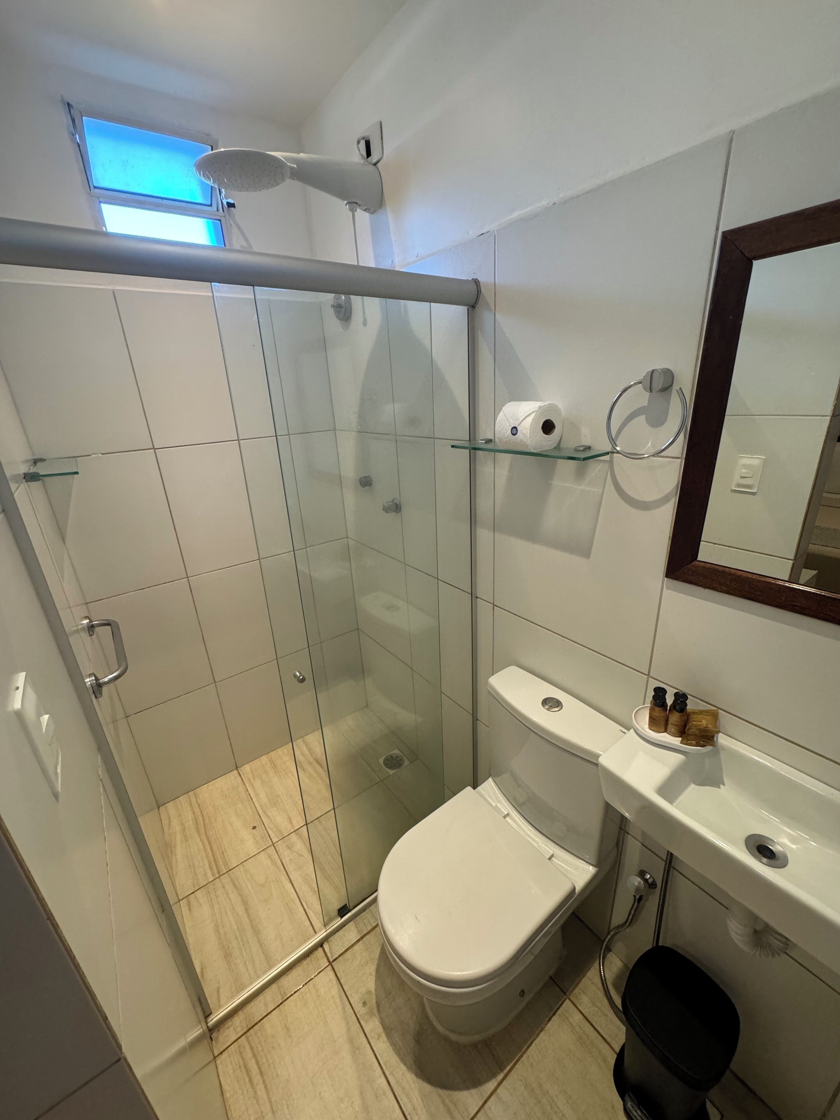 Een moderne badkamer met een glazen douchecabine, toilet, wastafel met zeepdispensers en een spiegel boven de wastafel.