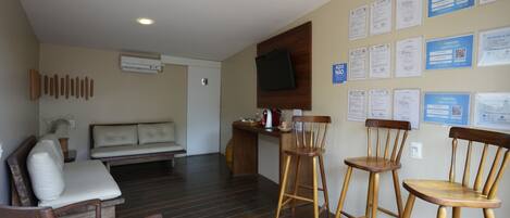 A room with a wooden floor, a sofa, two wooden chairs, a small table, and a wall-mounted TV.