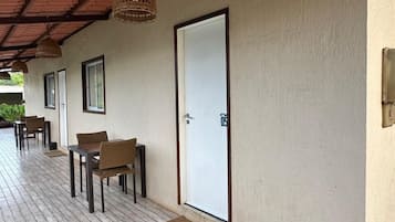 A covered outdoor area with wooden flooring, a door, and a table with chairs.