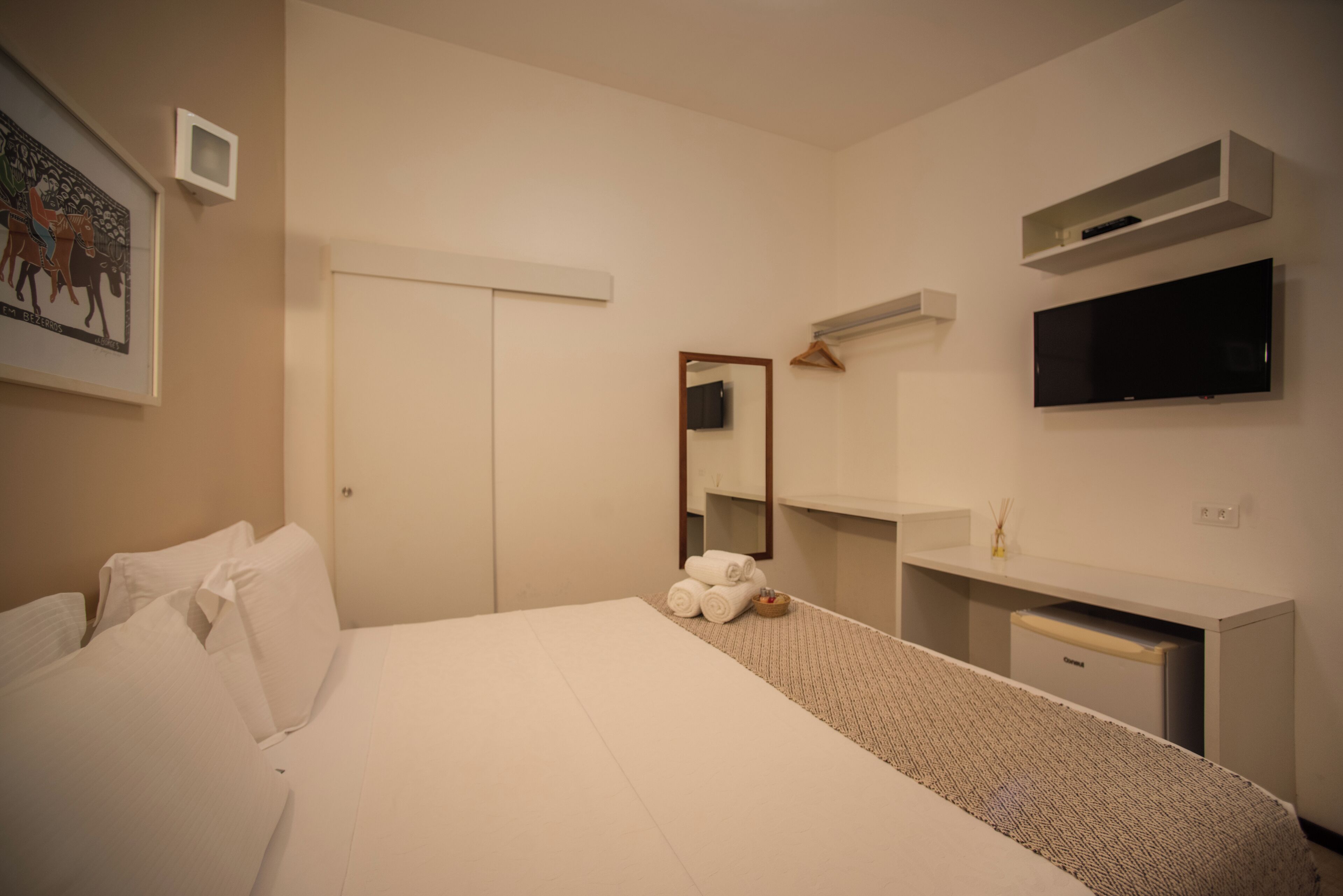 A hotel room with a bed, a desk, a television, and a mirror.