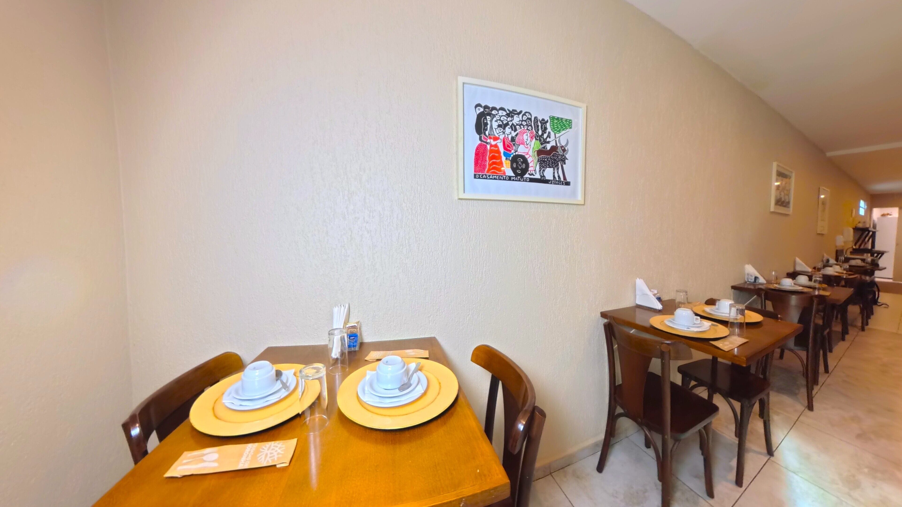 A hotel dining area with multiple tables set for dining, chairs, and a framed artwork on the wall.