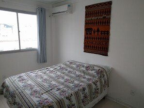 Een slaapkamer met een bed, een raam met gordijnen, een airconditioner en een wandtapijt.
