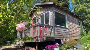 A wooden cabin with a balcony, surrounded by a garden with various plants and flowers.