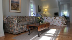 Een woonkamer met een bloemenbank, een houten salontafel, een bed met bloemenbeddengoed, een televisie en een schilderij aan de muur.