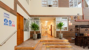 Eine Hotelhalle mit einer Treppe zum Obergeschoss, Zimmerpflanzen und einer Rezeption.