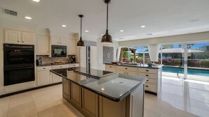 Una cocina moderna con una isla central, electrodomésticos integrados y vistas a una piscina.