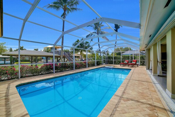 Une piscine à l’eau d’un bleu limpide, entourée d’une terrasse en bois et surmontée d’une structure métallique blanche.