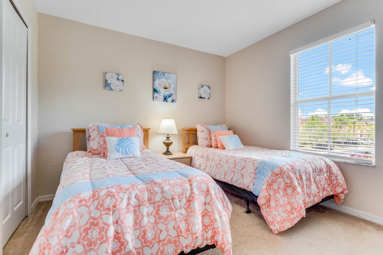 A bedroom with two beds, a nightstand with a lamp, and a window with blinds.