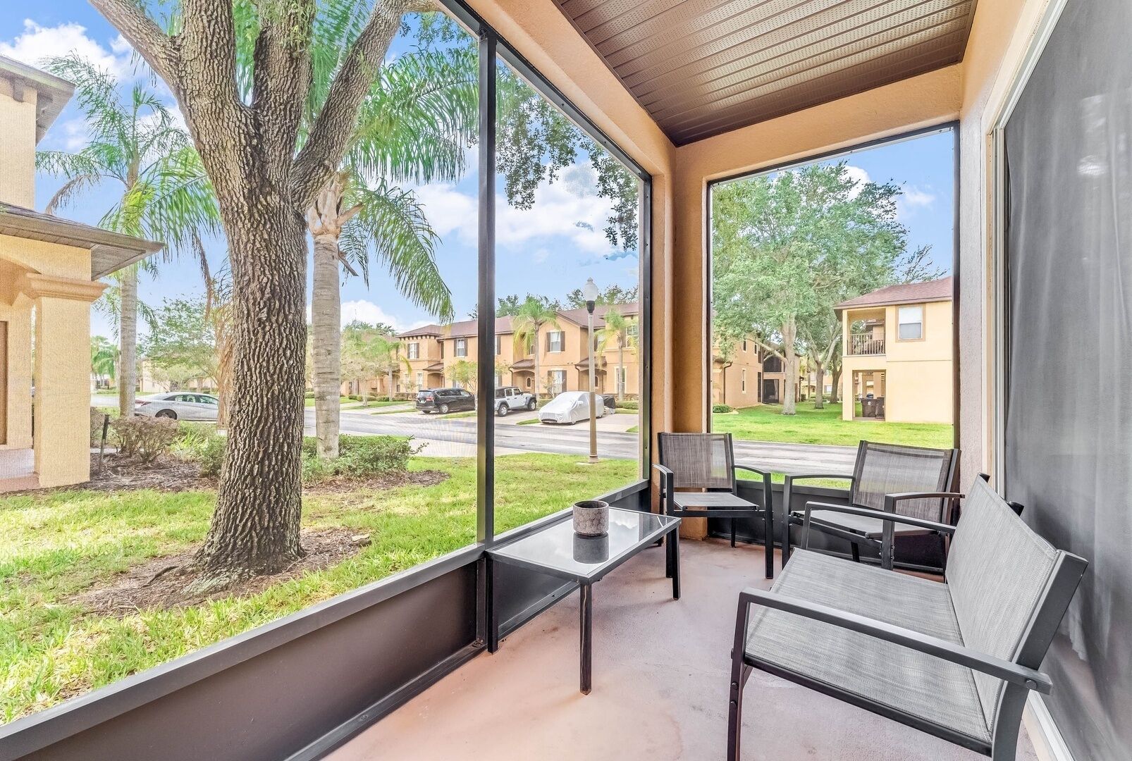 A balcony with a table and chairs, overlooking a residential area with houses and a tree.