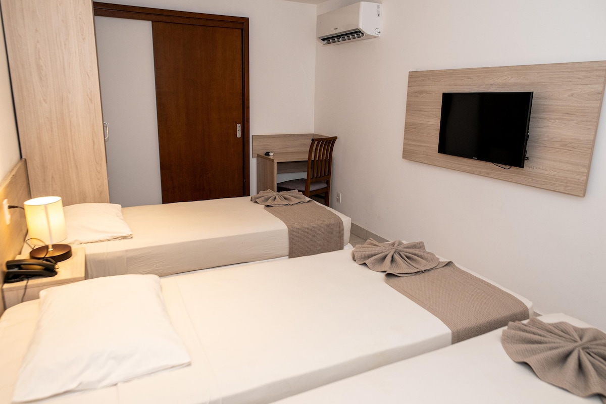 Habitación de hotel con dos camas individuales, un escritorio, una silla, un televisor montado en la pared y un equipo de aire acondicionado.