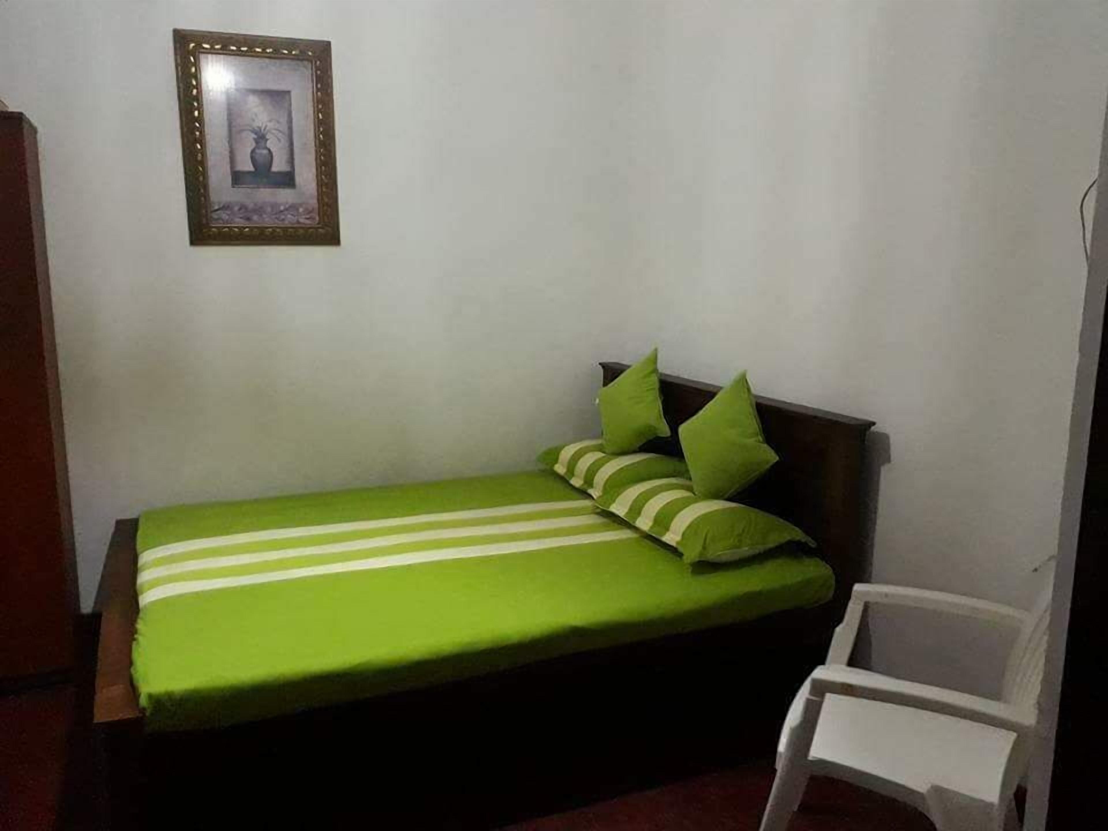 A small, single-bed room with a green-striped bedspread, a wooden headboard, and a white chair.