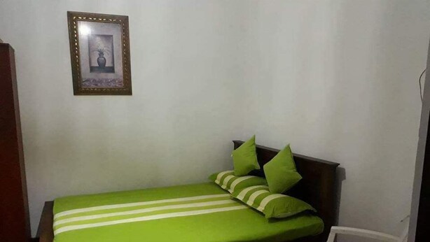 A small, single-bed room with a green-striped bedspread, a wooden headboard, and a white chair. - Villa Lagoonedge (Dodanduwa)
