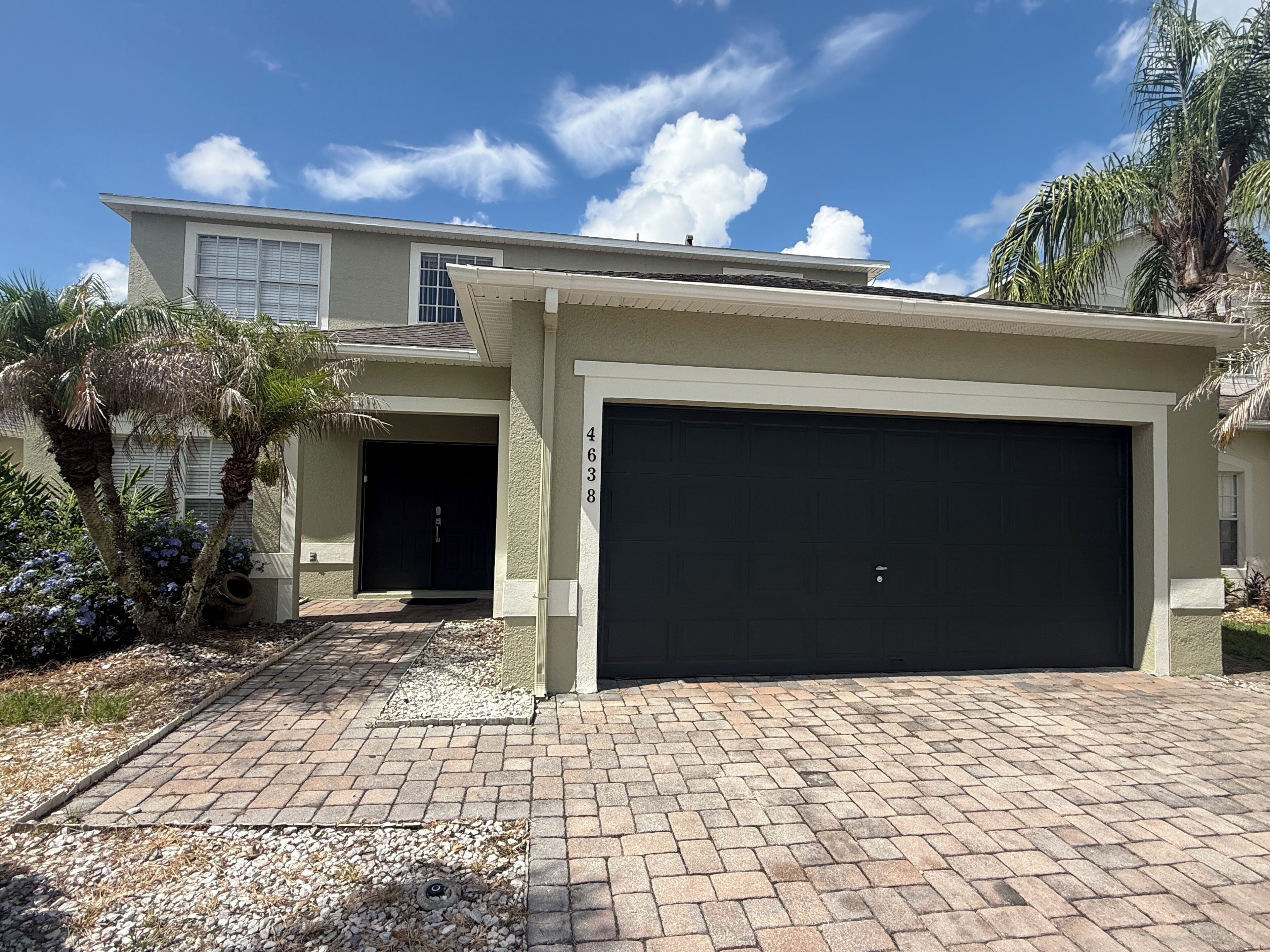A two-story house with a garage, a paved driveway, and a palm tree.