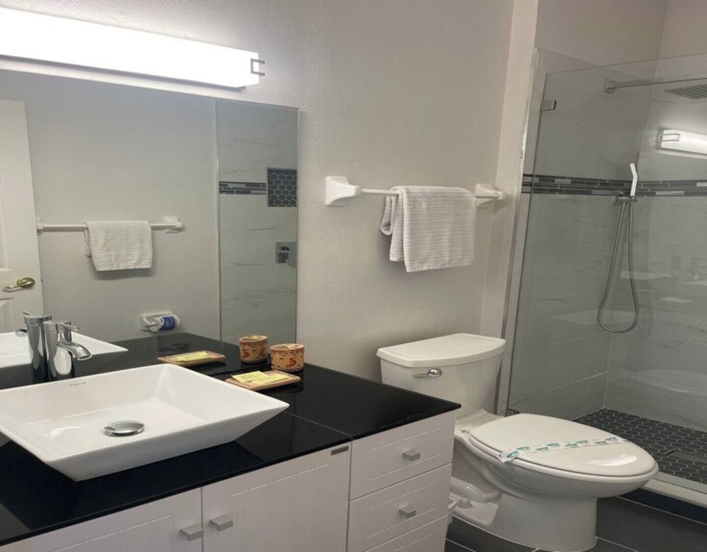 A modern bathroom with a white sink, black countertop, white toilet, and a glass shower enclosure.