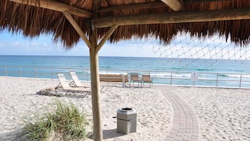 Relax on the beach with lounge chairs and a bench, shaded by a thatched-roof structure.