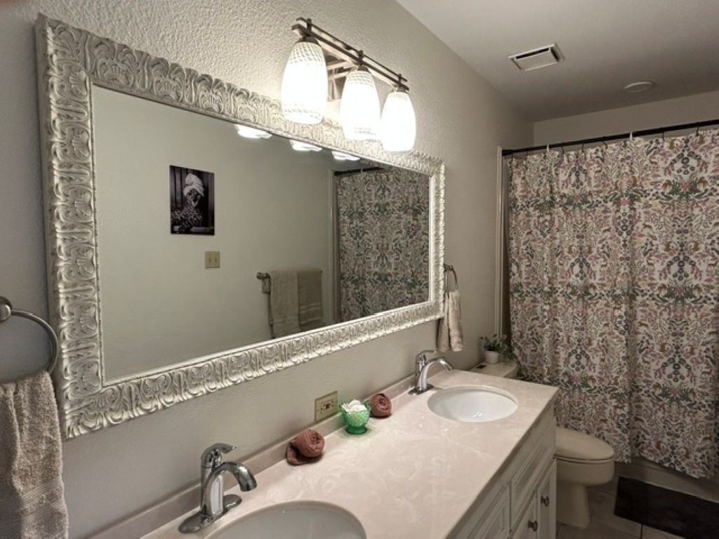 A bathroom with a large mirror, two sinks, and a toilet.