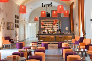 A bar area with orange and purple seating, a bar counter with various bottles, and a modern ceiling design with red pendant lights.