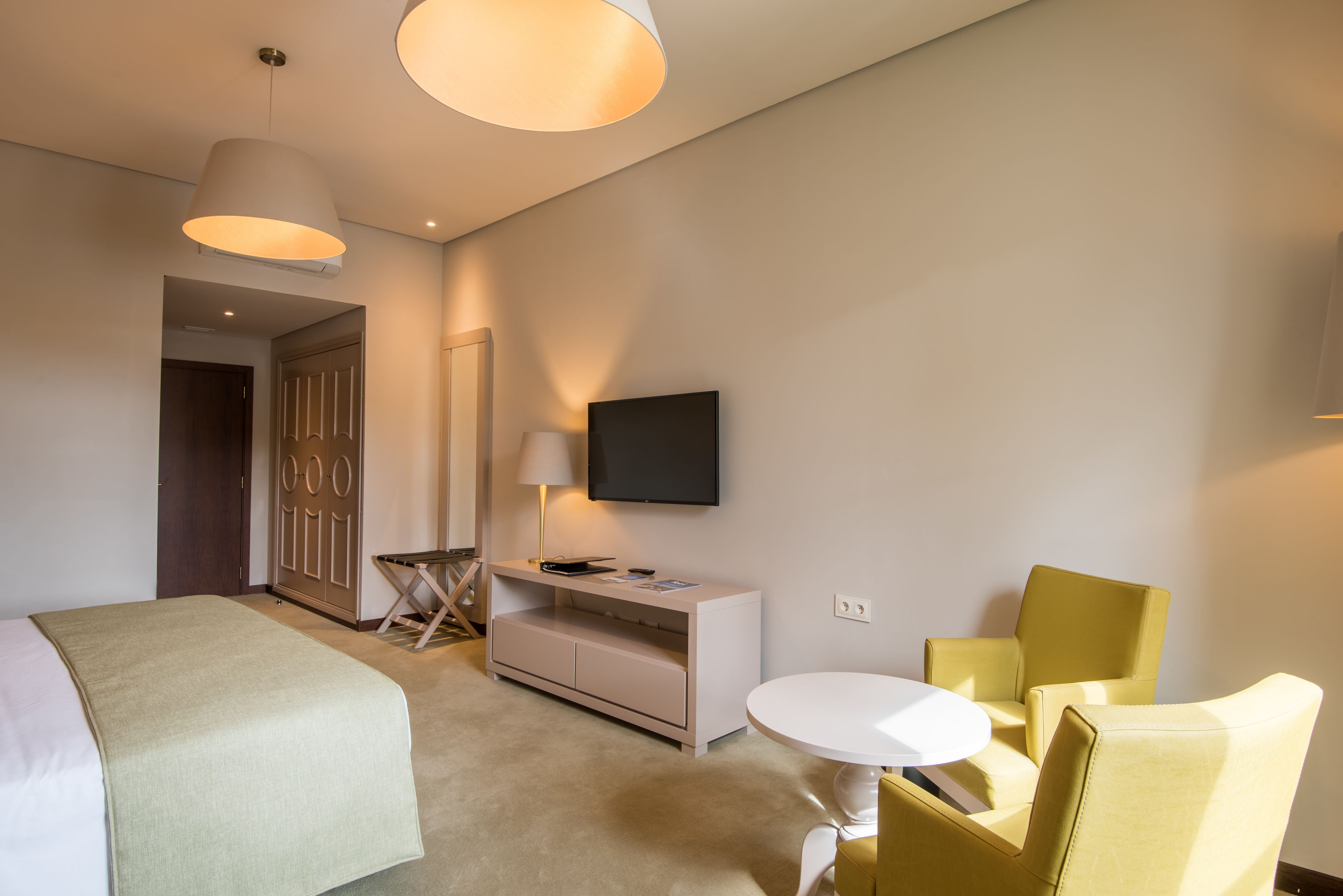 A hotel room with a bed, a desk with a lamp, a television, and two chairs.