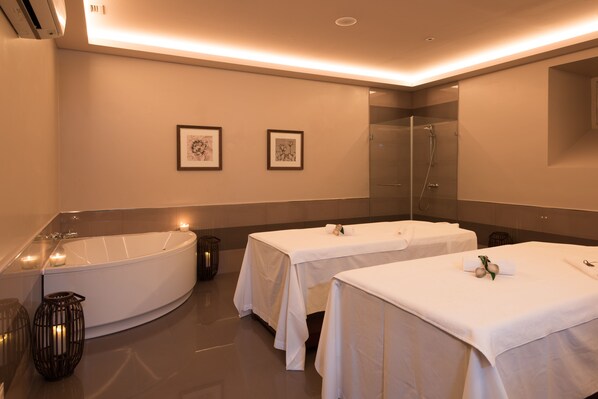 A modern spa room with a large bathtub, two massage tables, and framed artwork on the wall. - Vila Gale Collection Elvas Hotel (Elvas)