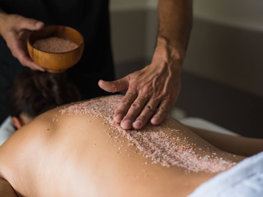 Une personne reçoit un massage du dos pendant que du sel est appliqué sur sa peau.