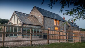 Un bâtiment en pierre doté d’une grande véranda en verre, d’une clôture en bois et d’une pelouse bien entretenue.