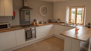 Une cuisine moderne avec des armoires blanches, un four encastré, un four à micro-ondes, une cuisinière à gaz et une grande fenêtre donnant sur l’extérieur.