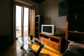 Sala de estar com mesa de centro de vidro, armários de madeira, televisão e varanda com vista.