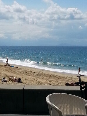 Vista de la playa con una silla en primer plano, arena y el océano.