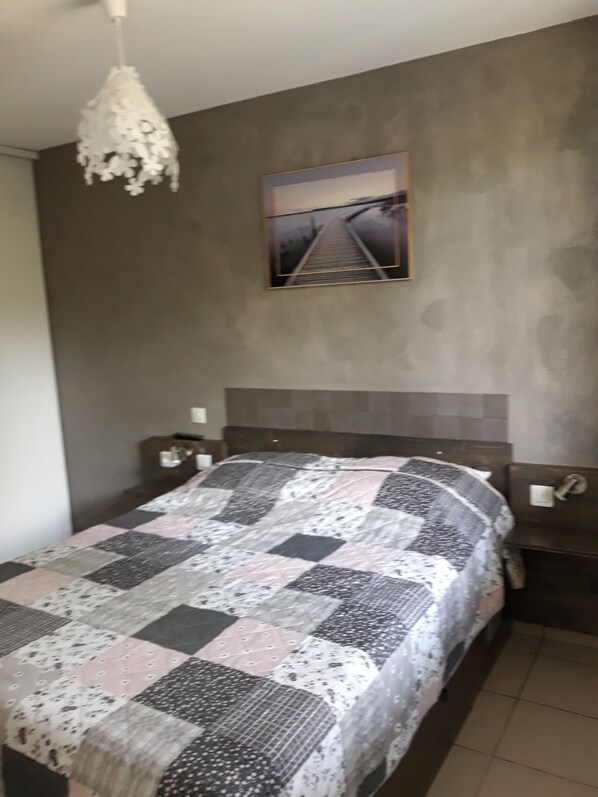 Un dormitorio con cama, mesita de noche, cuadro en la pared y lámpara colgante.