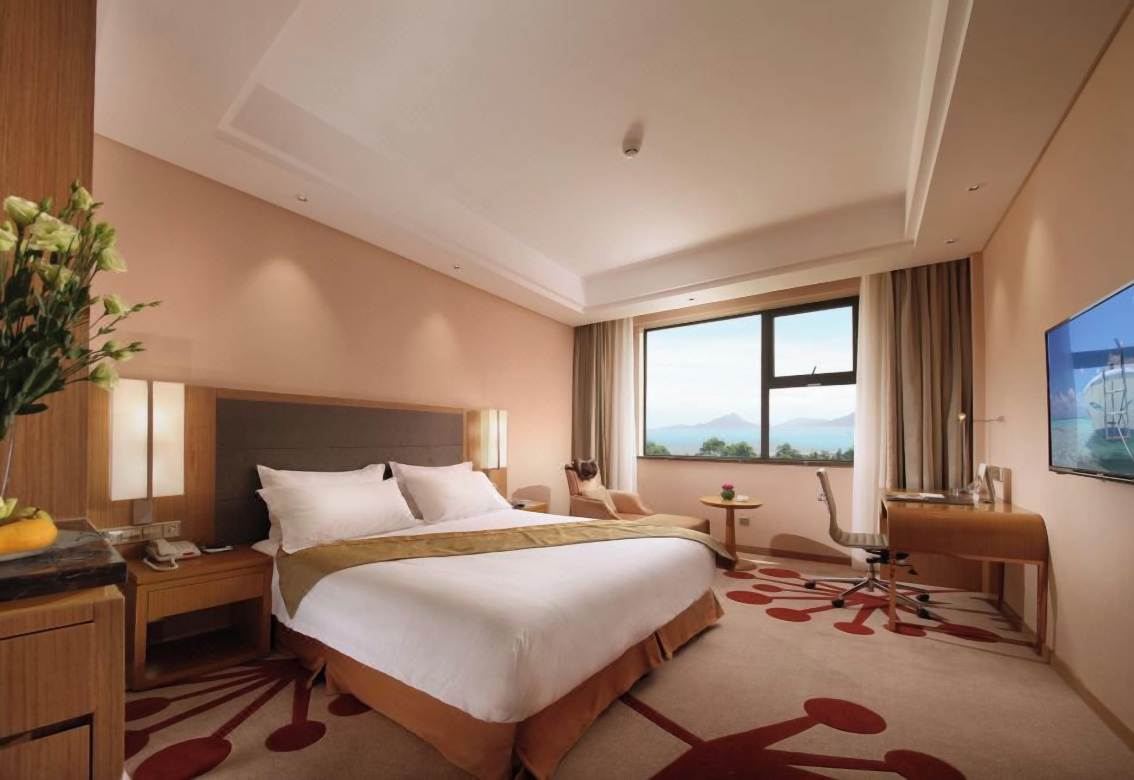 Une chambre d’hôtel avec un grand lit, un bureau, une chaise, une petite table et une fenêtre donnant sur un beau paysage.