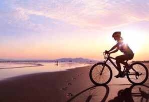 Una persona pedaleando en bicicleta en una playa con un atardecer de fondo.