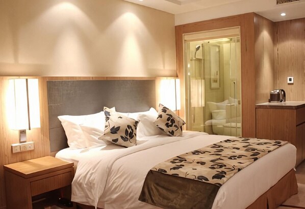 Una habitación de hotel con una cama, mesita de noche y baño con cabina de ducha de vidrio.