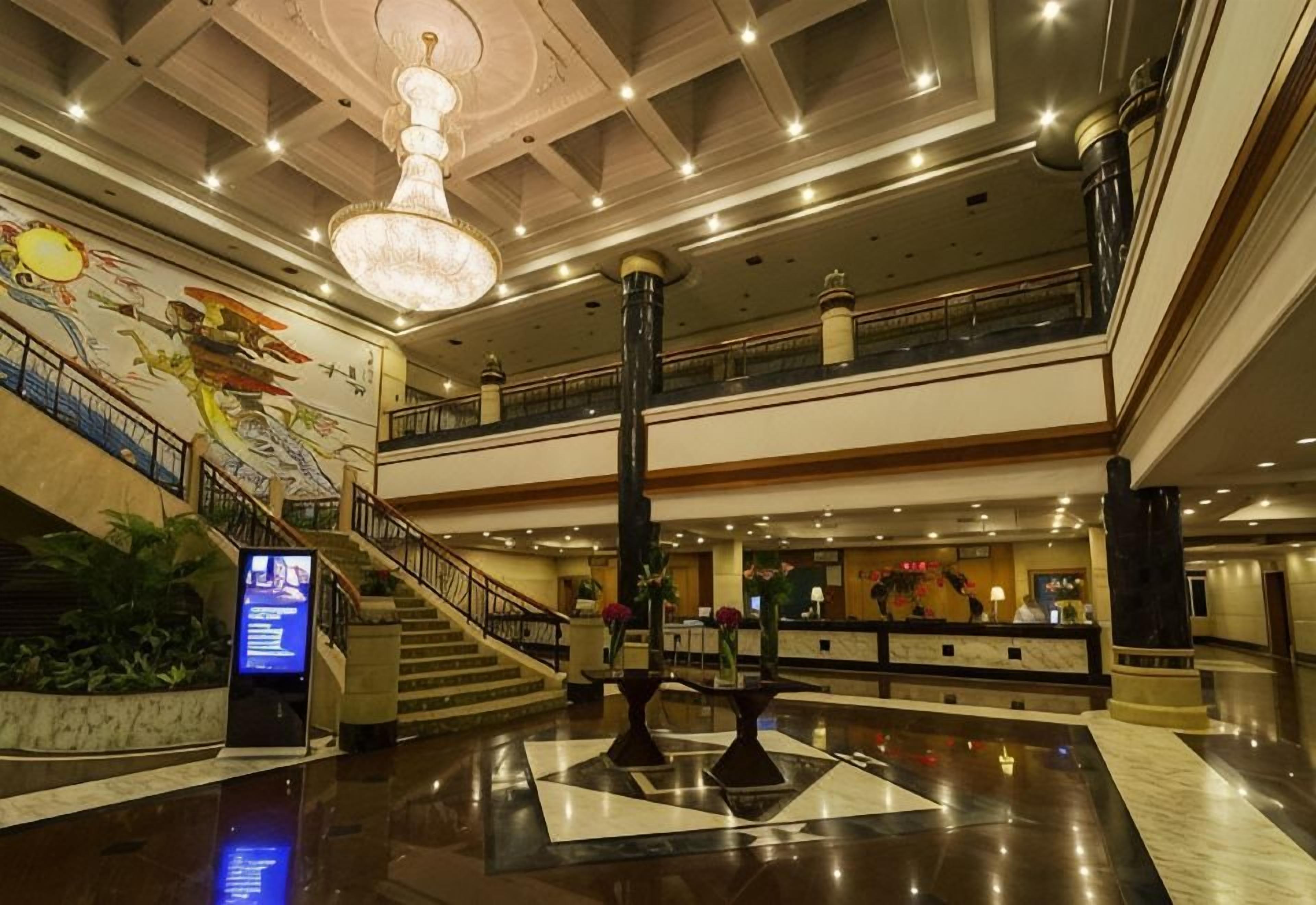 A spacious lobby with a grand chandelier, a reception desk, and a staircase leading to an upper level.