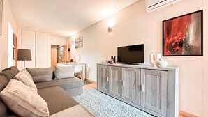 A modern living room with a grey sofa, a white coffee table, and a grey cabinet with a flat-screen TV. - Apartment with Terrace One bedroom for 2 people and a sofa bed for 2 people (Porto)