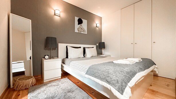 A modern bedroom with a large bed, bedside lamps, a nightstand, a mirror, and a wardrobe. - Apartment with Terrace One bedroom for 2 people and a sofa bed for 2 people (Porto)
