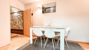 A dining area with a glass table, white chairs, a decorative wall piece, and a stone wall with a door. - Apartment with Terrace One bedroom for 2 people and a sofa bed for 2 people (Porto)