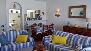 Una sala de estar con dos sofás a rayas, una zona de comedor con una mesa y sillas, y una cocina visible a través de un arco.