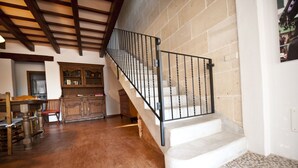 Un escalier avec une rampe en métal noir menant à un palier, un meuble en bois avec des portes en verre et une table à manger en bois avec des chaises.