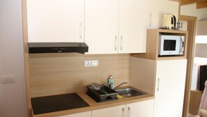 Una kitchenette compacta con microondas, estufa y un lavamanos pequeño.